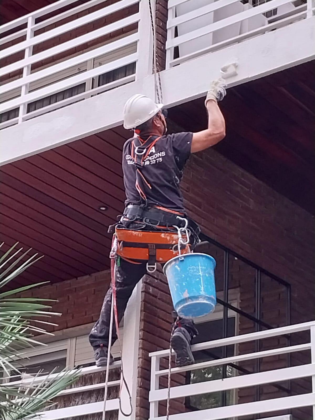 Técnico de ALTIUM pintando un balcón en altura, colgado de cuerdas y con arnés